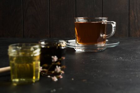 Cup of black tea in focus and two type of honey on foreground with dark background. Copy spaceの写真素材