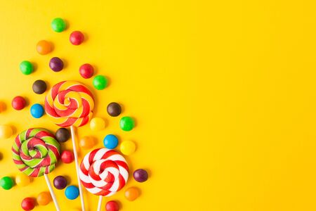 Three colorful round candies on sticks over yellow background with copy space. Top view. Flat lay. Closeup viewの写真素材