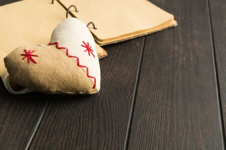 Soft toy with shape of heart with craft paper notebook over brown wooden table. Valentine's day concept. Symbol of love. Rustic style. Romantic conceptの写真素材