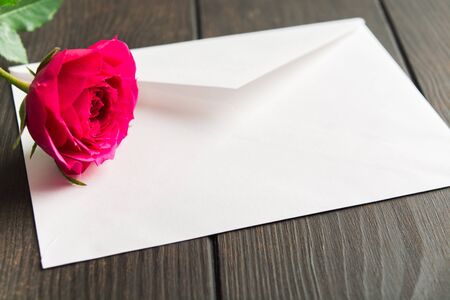 Beautiful pink rose lying on white envelope. Romantic sign with love letter. Selective focus. Valentine's day concept. Woman's day or Birthday present. Gift cardの写真素材