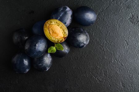 Black natural plums with mint over black textured background with copy space. Flat lay. Fresh blue fruits for vegetarian. Top viewの写真素材