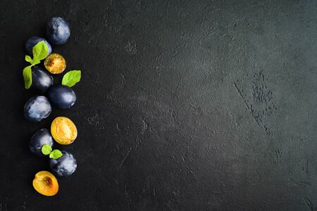 Organic fresh black fruit. Blue healthy plums with mint leaves and cutting fruits over black textured background. Copy space. Flat lay. Top viewの写真素材