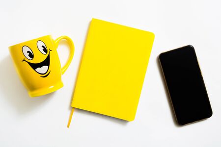 Yellow positive flat lay with notebook, cup and phone on white background for positive planning concept. Top view. Copy spaceの写真素材