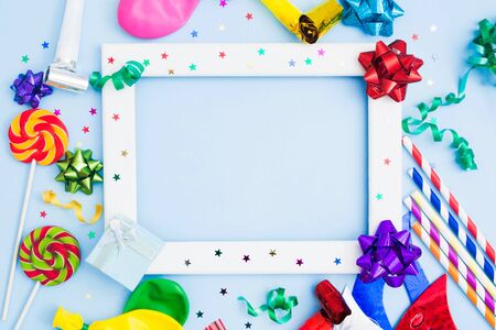 Brithday background with white wooden frame and colorful festive accessories. Copy space. Flat lay. Bows, lollipops, baloons, straws, streamers for holidaay conceptの写真素材