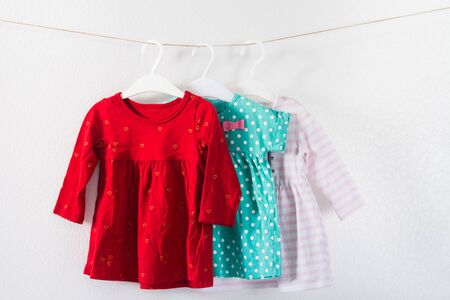 Three colorful summer dresses for baby girl on clothing hangers. Children clothes on white textured backgroundの写真素材