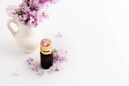 Dark bottle with golden cover and purple lilac on white background with copy space. Essential oil, perfume or chemistry liquid. Mock-upの写真素材