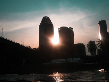 Beautiful sunset in city with view from the river with bridge. Sky, sun and silhouette of buildingsの写真素材