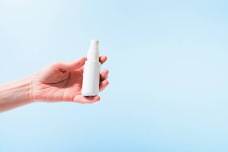 Plastic bottle with sanitizer in spray in female hand over blue background. Copy spaceの写真素材