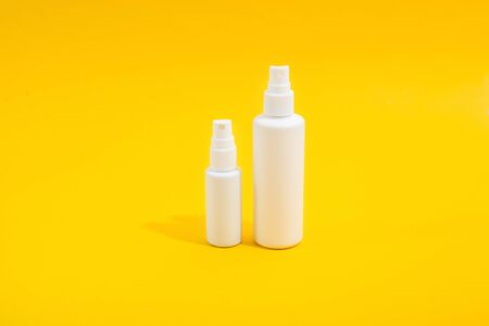 Two white plastic bottle with spray on yellow background. Sanitizer for home and mini version for hand bag. Copy space. Mockup for designの写真素材