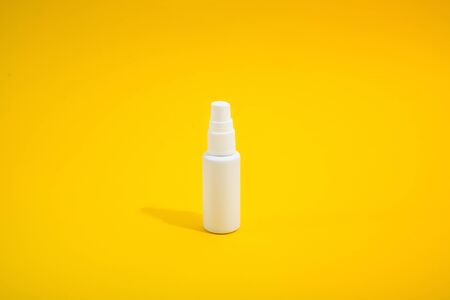 White smal plastic bottle with spray on yellow background with hard light. Mockup. Copy space. Medical antiseptic liquid for protection of virusの写真素材