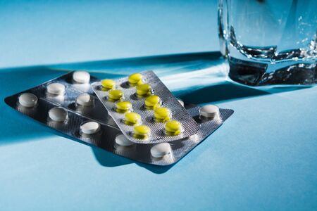 Two blister of pills with glass of water over blue background. Soft focus. Copy space. Tablets...