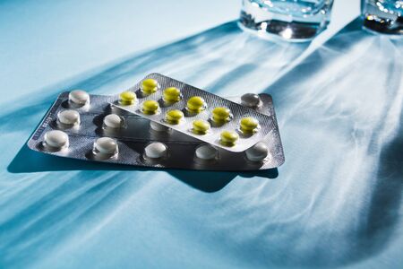 Two blister of pills with glass of water over blue background. Hard light. Selective focus. Pharmacy...