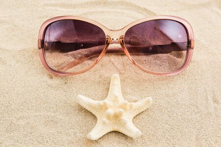 Funny face with sunglasses and sea star over sand background. Selective focusの写真素材