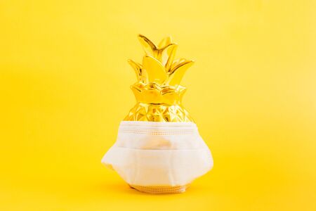 Golden pineapple with medicine mask on yellow background. Summer prevention concept. Copy space. Epidemic concept in vacationの写真素材