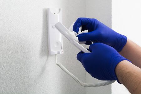 Man in blue gloves cleaning with tissue intercome or door phone in flat. Cleaning interior like preventive measurement of covid-19. Protection of viruses conceptの写真素材