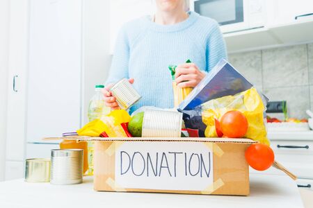 Donation food in cardboard box with woman in kitchen. Help for people in quarantine time. Charity conceptの写真素材