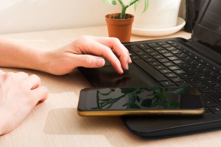 Woman hands with laptop and phone on table. Remotely work at home. Distance work
