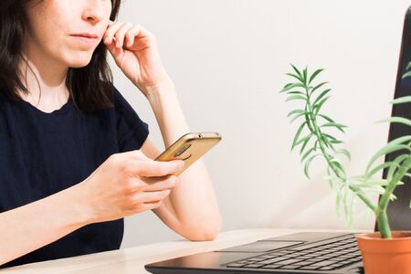 Beautiful young woman with dark hair sitting at table with laptop and using phone. Online business with social network. Remote work conceptの写真素材