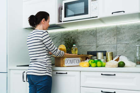 Donation food in cardboard box with caucasian woman with dark hair in kitchenの写真素材