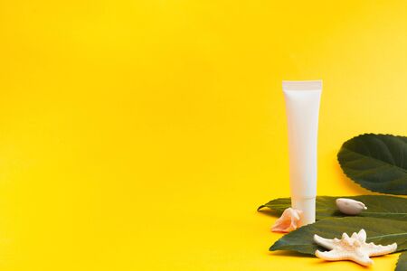 Mockup white tube with sea star and green leaf on yellow background. Copy spaceの写真素材