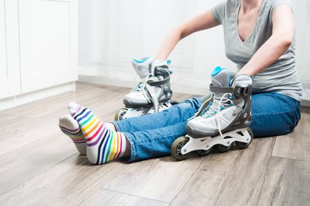 Woman in jeans and colorful socks sitting on floor at home with arms in roller skates....