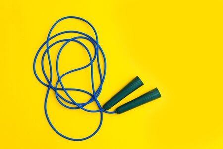 Sport cardio activity equipment. Blue fitness skipping rope for jumping with plastic handles on yellow background. Flat lay. Top view. Copy spaceの写真素材