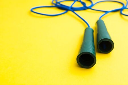 Sport cardio activity equipment. Blue fitness skipping rope for jumping with plastic handles on yellow background. Selective focus. Copy spaceの写真素材
