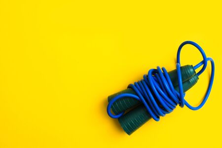 Sport cardio activity equipment. Blue fitness skipping rope for jumping with plastic handles on yellow background. Top view. Flat layの写真素材