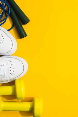 White sneakers, dumbbells and skipping rope on yellow background. Flat layの写真素材