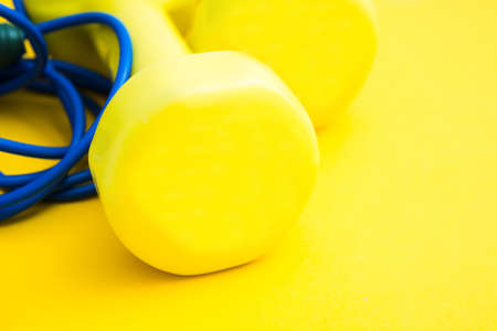 Yellow dumbbells and blue skipping rope on yellow background. Fitness conceptの写真素材