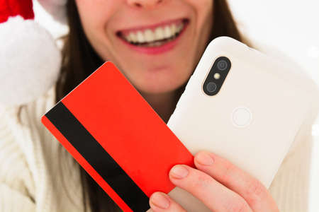 Croped beautiful smiling woman in Santa hat holding phone and bank plastic cardの写真素材