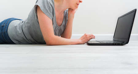 Faceless caucasian woman lying on floor and working with a laptopの写真素材