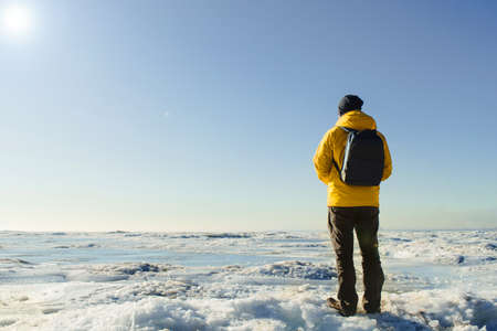 One faceless man in yellow raincoat with backpack standing on frozen sea. Natureの写真素材