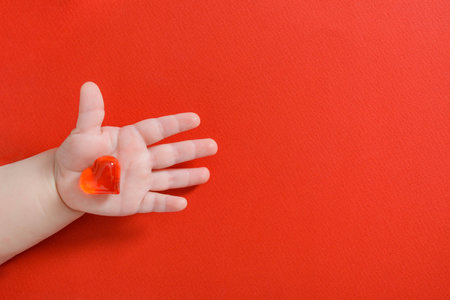 Red heart in newborn baby hand on red background with copy space. Flat layの写真素材