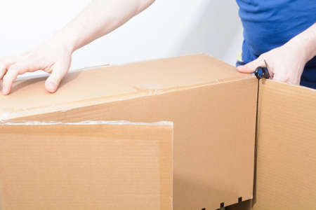 Caucasian man holding sharp steel box cutter knife with open cardboard boxの写真素材
