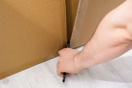 Caucasian man hand cutting a cardboard box with sharp cutter knifeの写真素材