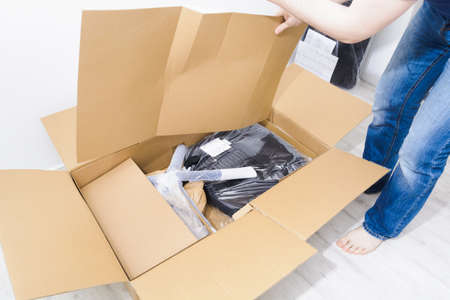 Faceless caucasian man standing in jeans at home and open box with office chairの写真素材