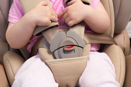 Faceless small baby sitting in special car seat with safety seatbeltsの写真素材
