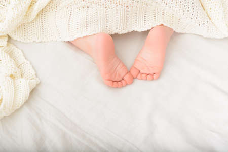 Feet of sleeping child in bed. Sweet baby part covered with soft blanketの写真素材