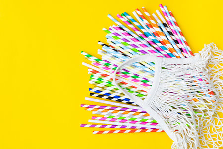 Colorful paper straws in material bag on yellow background with copy spaceの写真素材