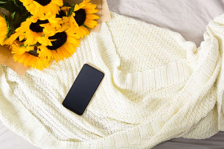 Bouquet of yellow sunflowers with phone on fabric white plaid backgroundの写真素材