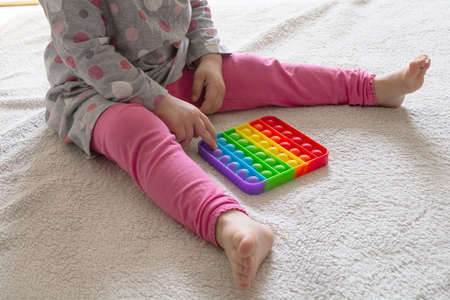 Young little girl sitting on rug at home and playing with new trendy toy Pop Itの写真素材