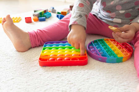 Young little girl sitting on rug at home and playing with new trendy toy Pop Itの写真素材