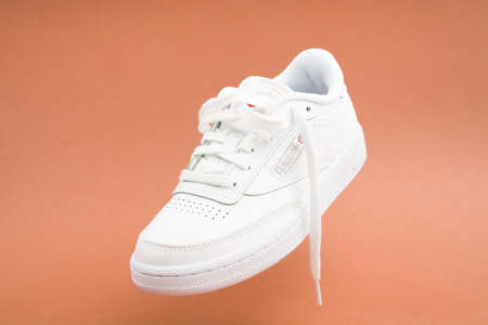 Levitation of single female stylish white casual sneaker on brown backgroundの写真素材