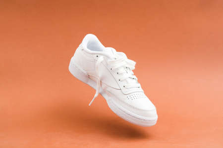 Levitation of single female stylish white casual sneaker on brown backgroundの写真素材