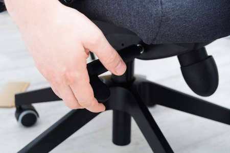 Man checks lifting mechanism of chair. Assembling office chair indoorsの写真素材
