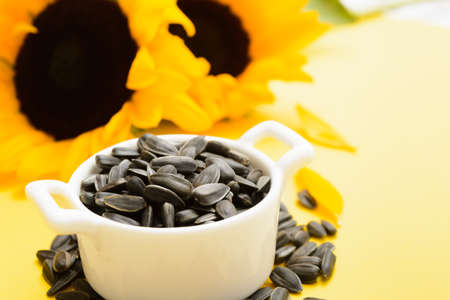 Closeup view of black sunflower seeds in white ceramic bowl with flowersの写真素材