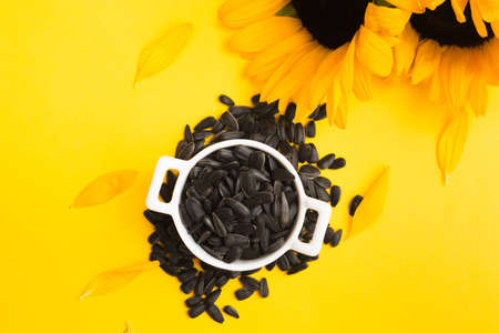 Top view of black sunflower seeds in white ceramic bowl with flowersの写真素材