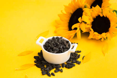 Closeup view of black sunflower seeds in white ceramic bowl with flowersの写真素材