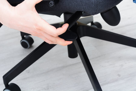 Man checks lifting mechanism of chair. Assembling office chair indoorsの写真素材